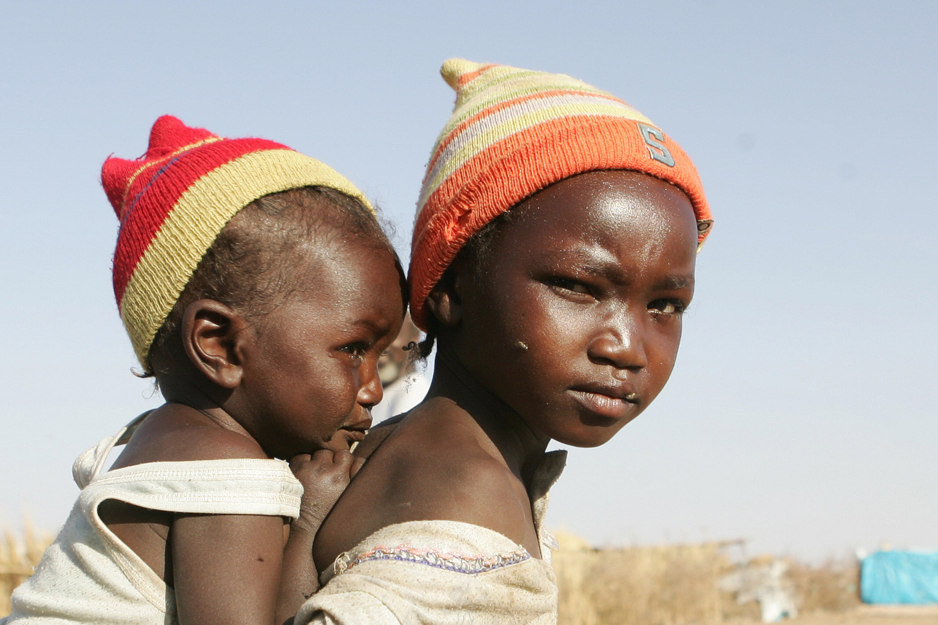 A displaced Sudanese girl carries her sister at the Otach Displaced Persons camp in the city of Nyala, in Sudan’s strife-torn Darfur region, 22 February 2007.